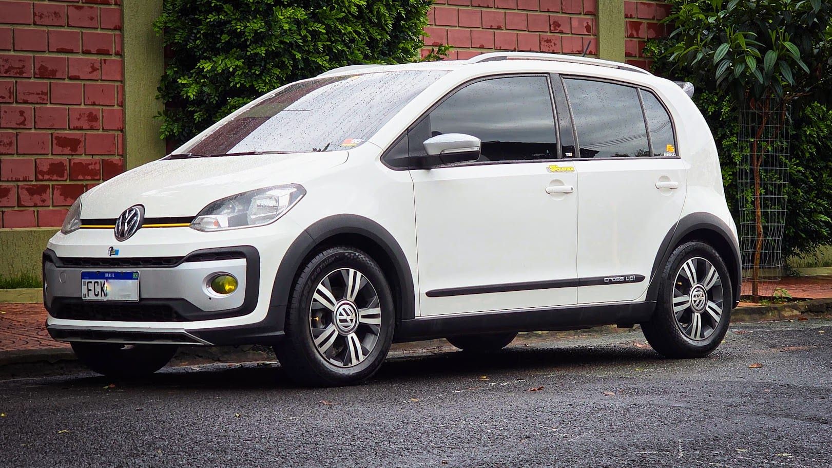 Volkswagen Cross Up! TSI branco estacionado numa rua molhada, em frente a um muro de tijolos